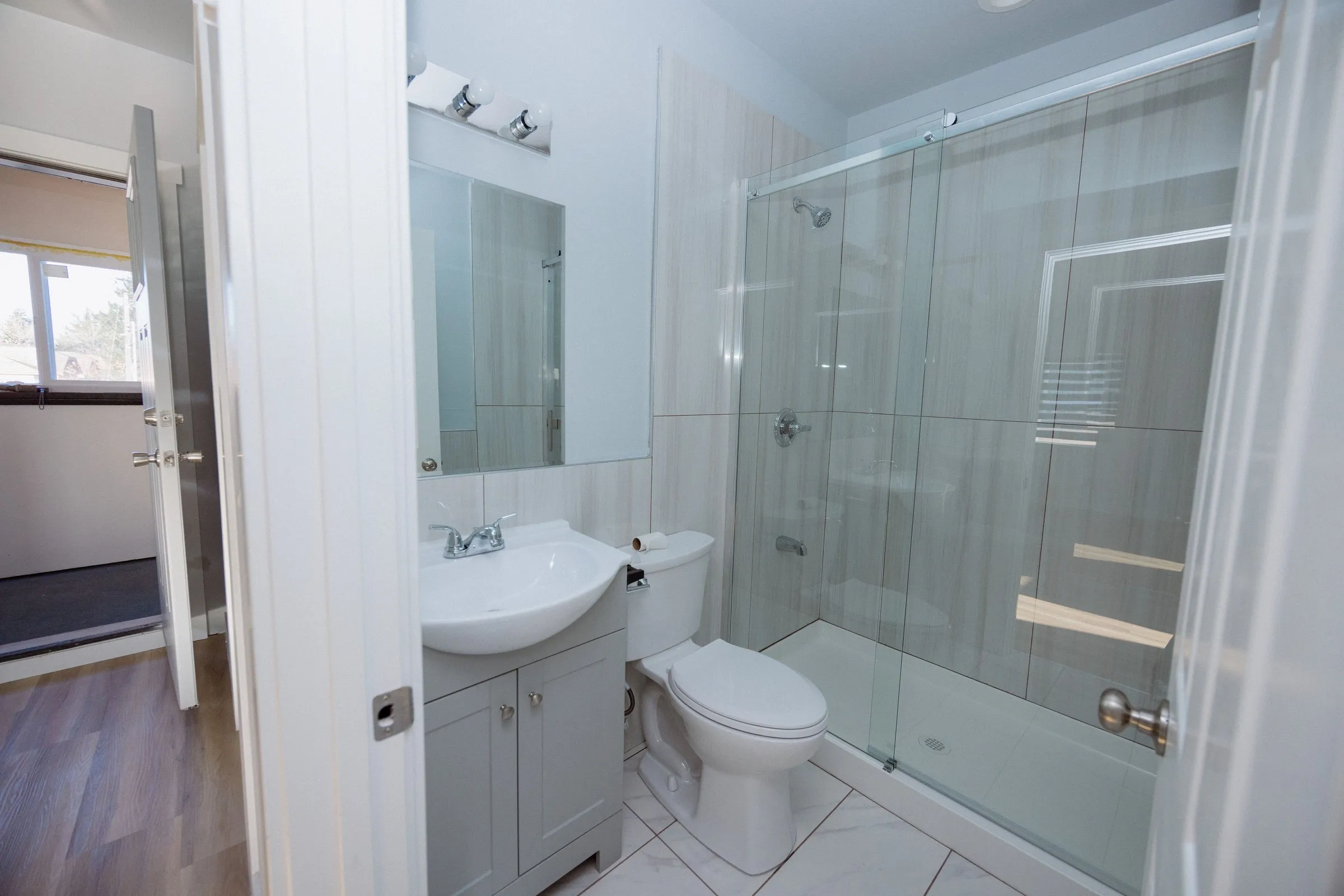 Bathroom with a glass-enclosed shower over a tiled surround and a compact vanity